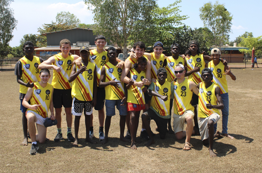 A group of students from Tiwi College and 鶹ýAV in AFL jumpers smiling and looking towards the camera