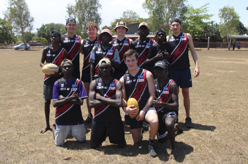 A group of students from Tiwi College and 鶹ýAV in AFL jumpers smiling and looking towards the camera